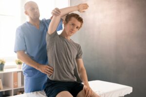 Mature physiotherapist in uniform supporting arm of patient during sidebends
